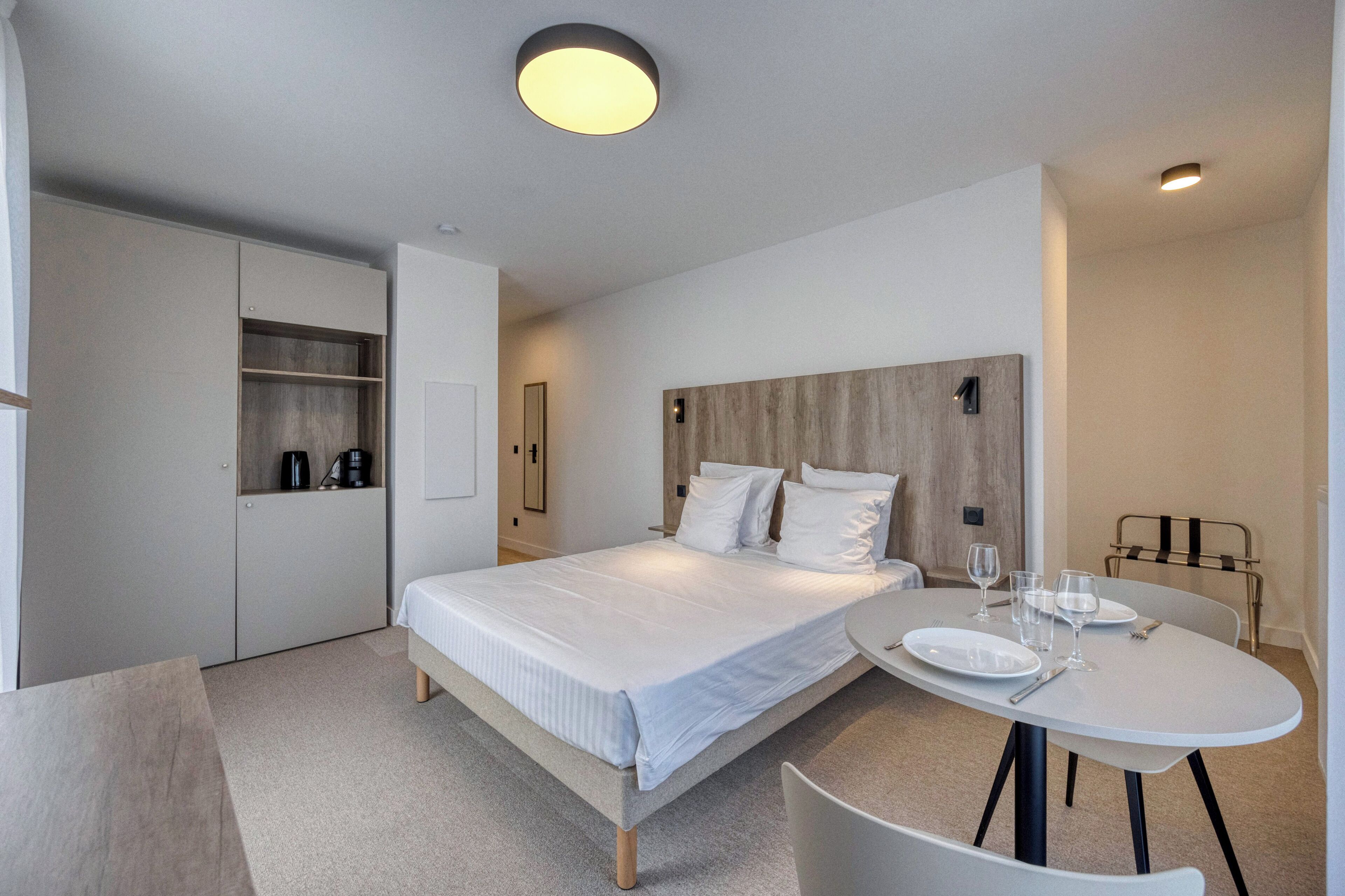 A modern bedroom with a bed, bedside table, and a round dining table with chairs.