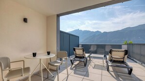 A balcony with a table and chairs, a view of mountains, and a potted plant.