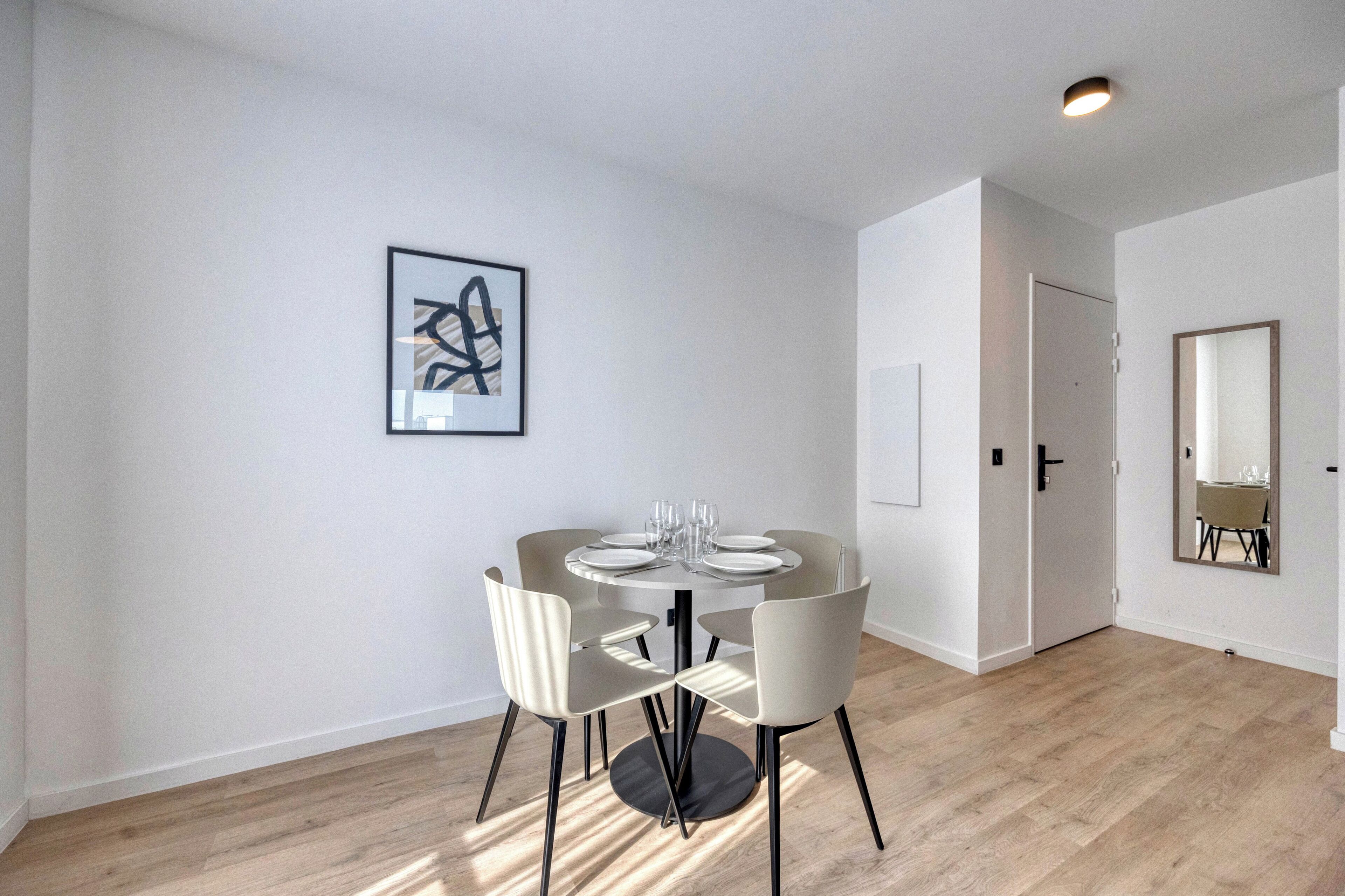 Ein moderner Essbereich mit einem runden Tisch und vier Stühlen, einem gerahmten abstrakten Kunstwerk an der Wand und einer Tür zu einem anderen Raum.