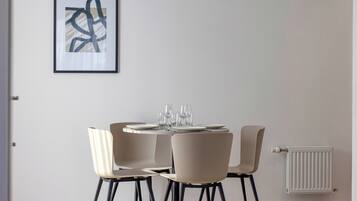 A dining area with a round table set for four, four chairs, and a framed abstract painting on the wall.