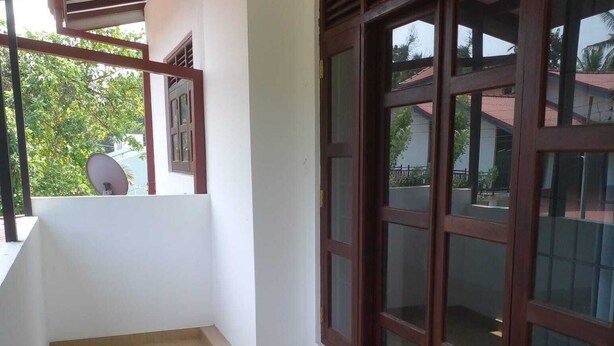 A corridor with a tiled floor, a white wall, and a large window with a dark frame. - Villa in Yakkala, Gampaha (Yakkala)