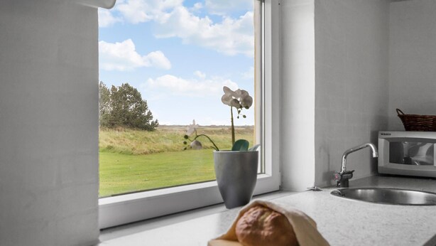 A kitchen with a window view of a grassy field and trees, a microwave, a sink, and a loaf of bread on a cutting board. - Stunning home in Ribe with Wi-Fi (Ribe)