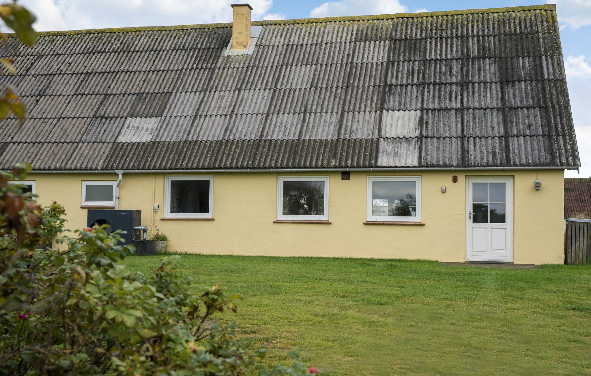 A two-story house with a corrugated metal roof, a small front yard, and a single door.