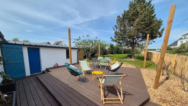 Un patio in legno con mobili da esterno, tra cui sedie e un tavolo, circondato da una recinzione e alberi.