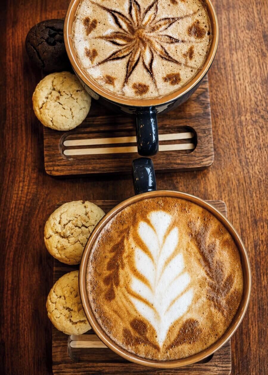 Two cups of coffee with latte art on a wooden surface, accompanied by cookies.