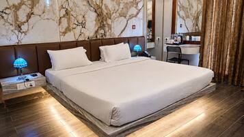 A modern hotel room with a large bed, a ceiling fan, marble-patterned walls, and a wooden floor.