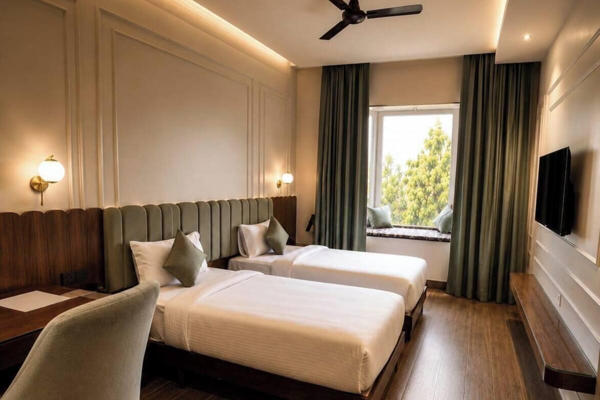 Habitación de hotel con dos camas, ventilador de techo, televisión y ventana con cortinas.