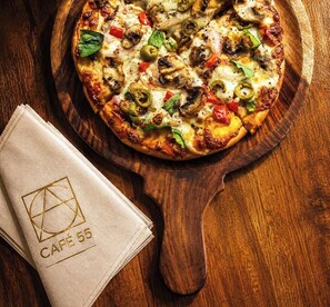 Eine Pizza auf einem Holzbrett mit einer Serviette, auf der 'CAFÉ 55' steht.