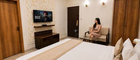 A bedroom with a large bed, a television mounted on the wall, a wardrobe, and a seating area with a sofa.