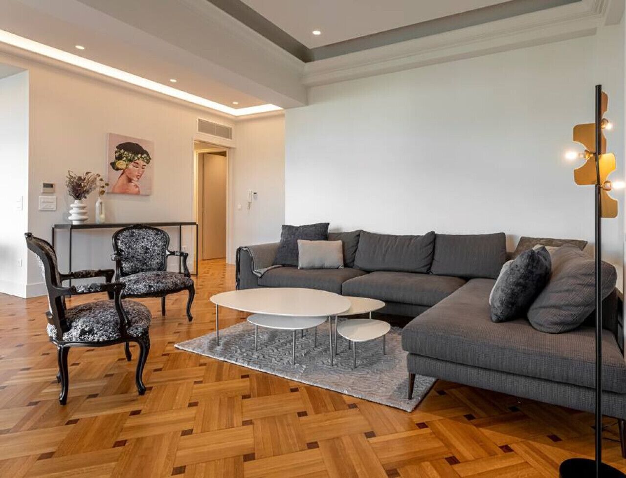 Ein modernes Wohnzimmer mit einem grauen Sofa, zwei Sesseln, einem Couchtisch und einer Stehlampe.