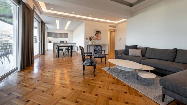 A spacious living area with a wooden parquet floor, a grey sofa, a white coffee table, and a dining area with a table and chairs. - Phaedrus Living: City Center Luxury Flat N. Kosmos (Athina)