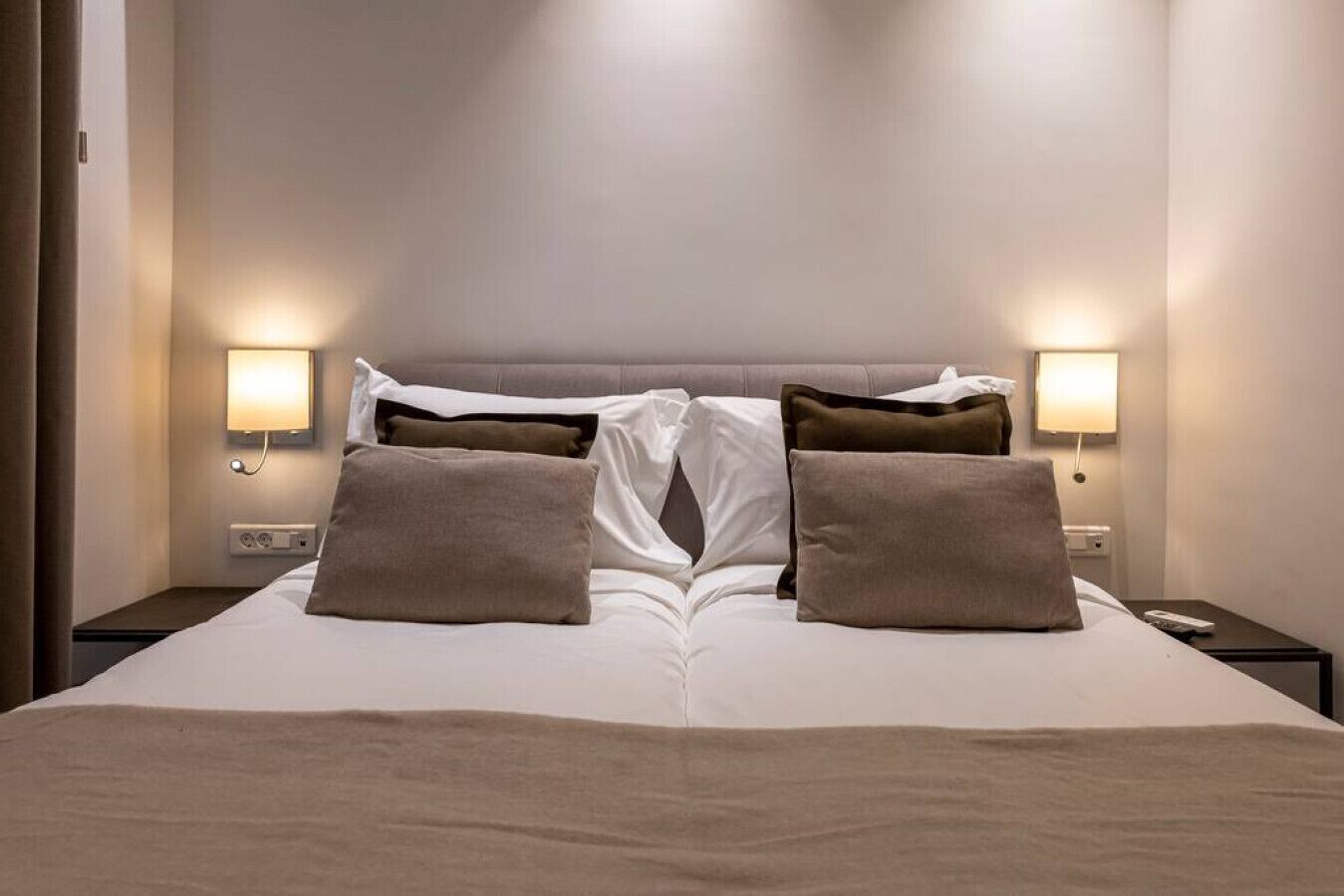 A neatly made bed with a headboard, two bedside lamps, and a nightstand with a power outlet.