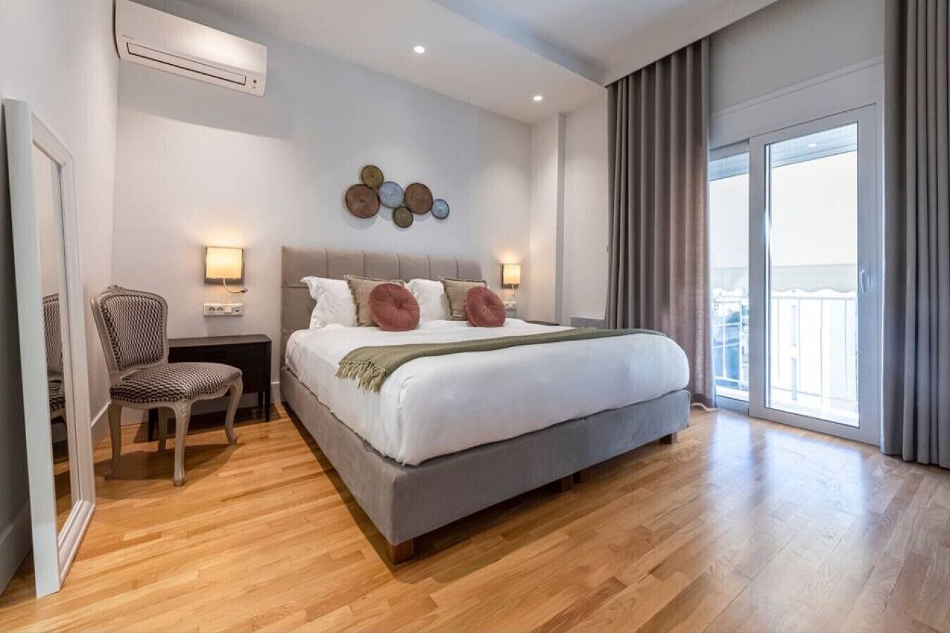 A modern bedroom with a large bed, a chair, a nightstand, and a wall-mounted light fixture.