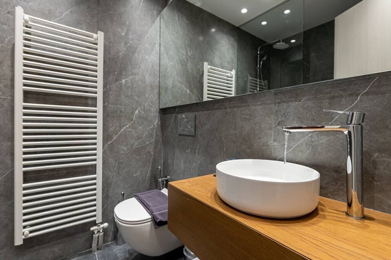A modern bathroom with a white toilet, a round sink with a chrome faucet, and a towel rack.