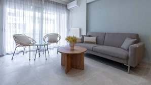Una sala de estar moderna con un sofá gris, dos sillas de mimbre, una mesa de centro redonda de madera y una planta en maceta.