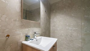 Un baño con lavamanos blanco, mueble de madera y un espejo encima.