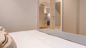 A bedroom with a bed, a bedside table, a wardrobe, and a small kitchenette in the background. - Phaedrus Living: Executive Flat Kolonaki (Athina)