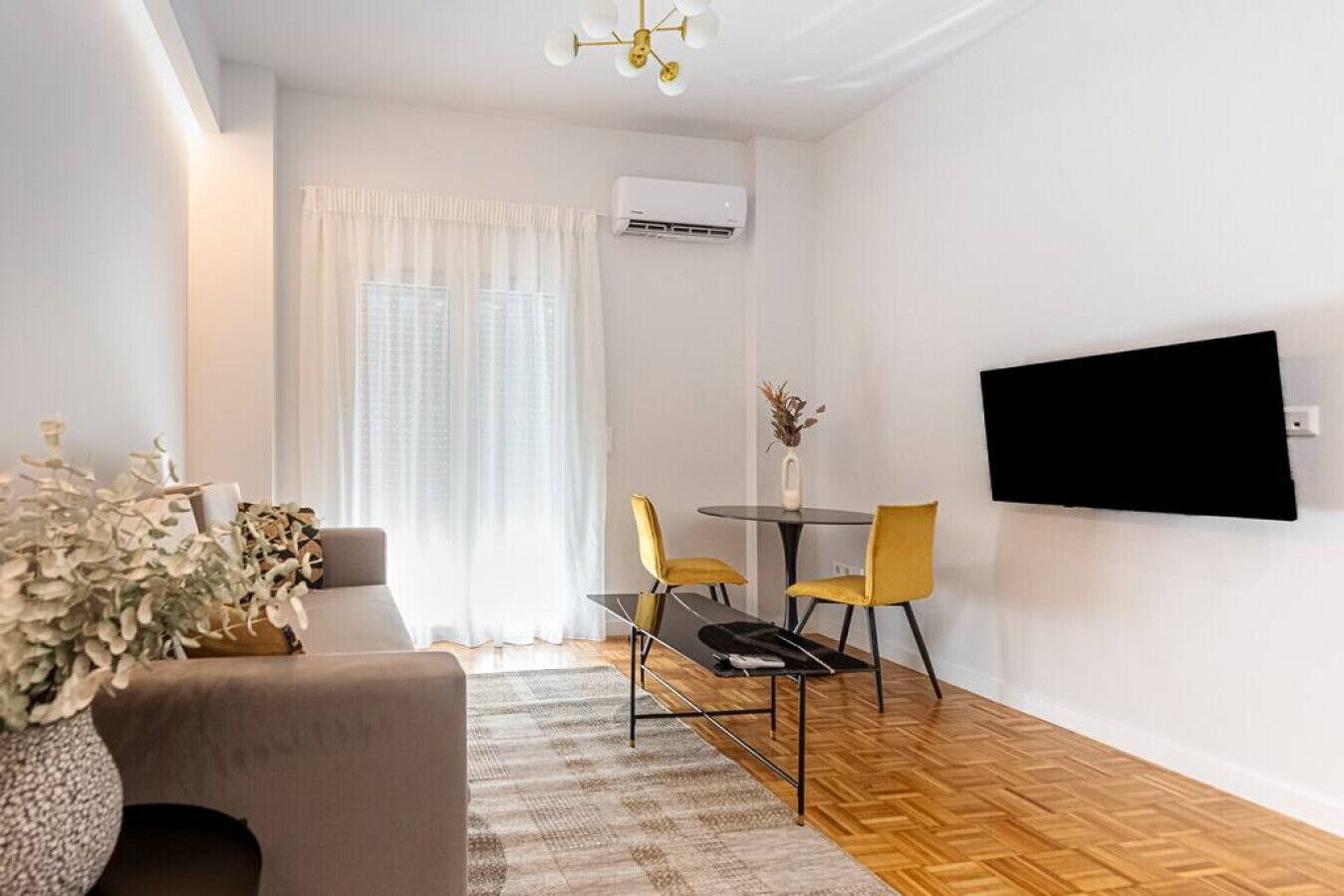 Un salon moderne comprenant un canapé, une table à manger avec des chaises, un téléviseur à écran plat fixé au mur et un appareil de climatisation.