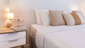 A neatly made bed with white and beige pillows, a bedside table with a lamp and books, and a simple wall-mounted power outlet. - Phaedrus Living: Luxury Flat Panormou (Athens)