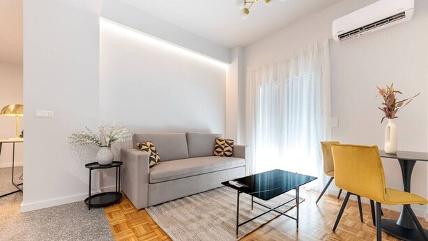 A modern living room with a grey sofa, a black coffee table, and a yellow chair. There is a small side table with a vase of flowers. - Phaedrus Living: Luxury Flat Panormou (Athens)