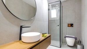 A modern bathroom with a round mirror, a wooden vanity, a white sink, and a glass shower enclosure. - Phaedrus Living: Luxury Flat Panormou (Athens)