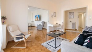 A modern living room with a sofa, a rocking chair, a dining table, and a kitchen area in the background.