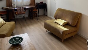 A cozy living room with a wooden floor, a sofa, a dining table with chairs, and a hanging light fixture.