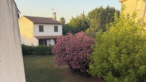 A residential area with a gravel driveway, a pink flowering bush, and a white building with a tiled roof.