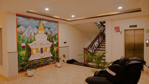 A hotel lobby with a mural of a mountain and temple, a staircase, an elevator, and a reception area with a sofa and potted plants. - The Z Retreat and Spa (Gangtok)
