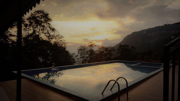 A swimming pool with a view of a sunset and surrounding hills. - The Z Retreat and Spa (Gangtok)