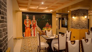 A restaurant with a traditional Asian theme, featuring a large mural of a couple in traditional attire, a patterned floor, and a brick wall. - The Z Retreat and Spa (Gangtok)