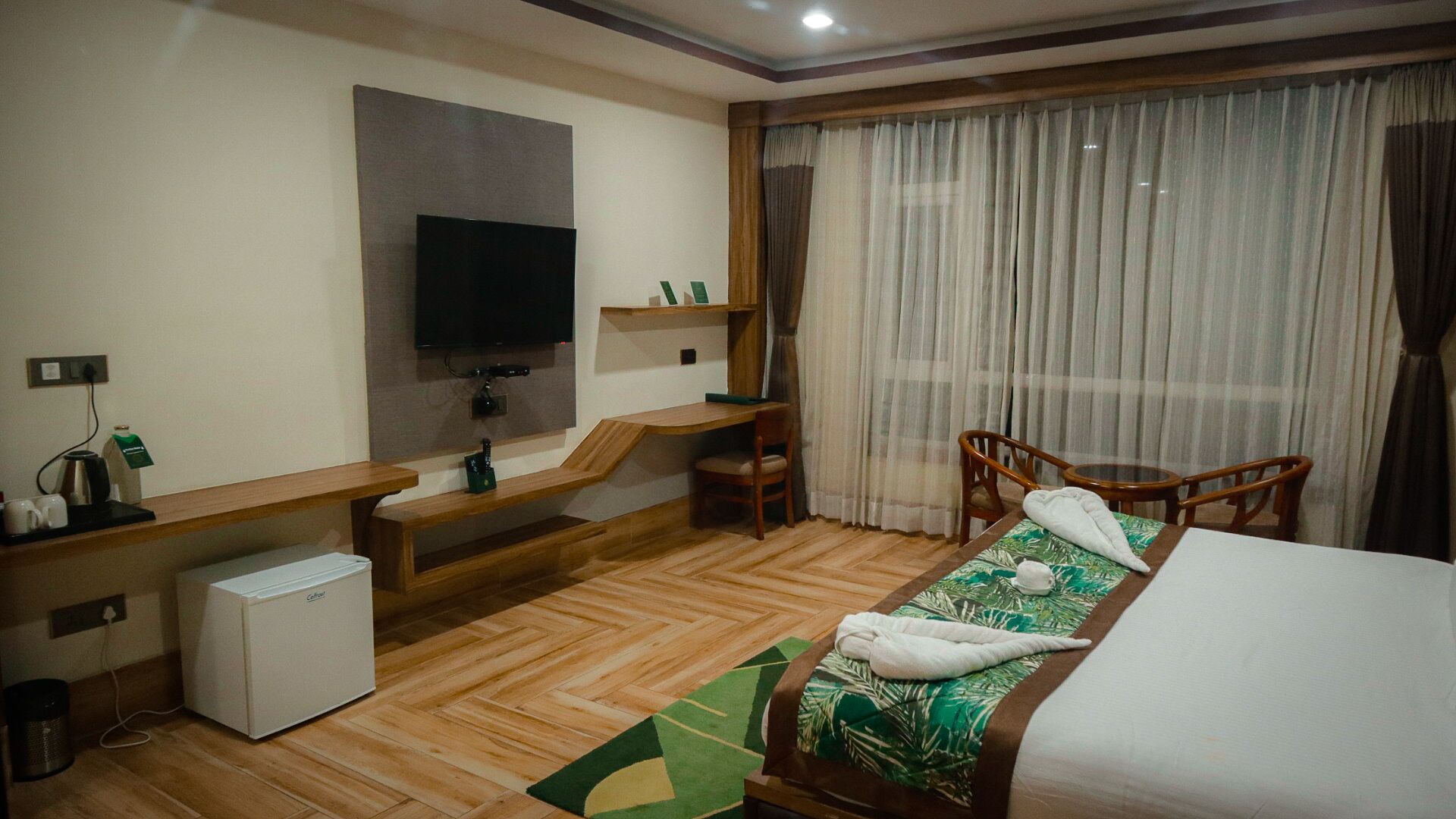 A hotel room with a bed, a desk, a chair, a television, and a small refrigerator.