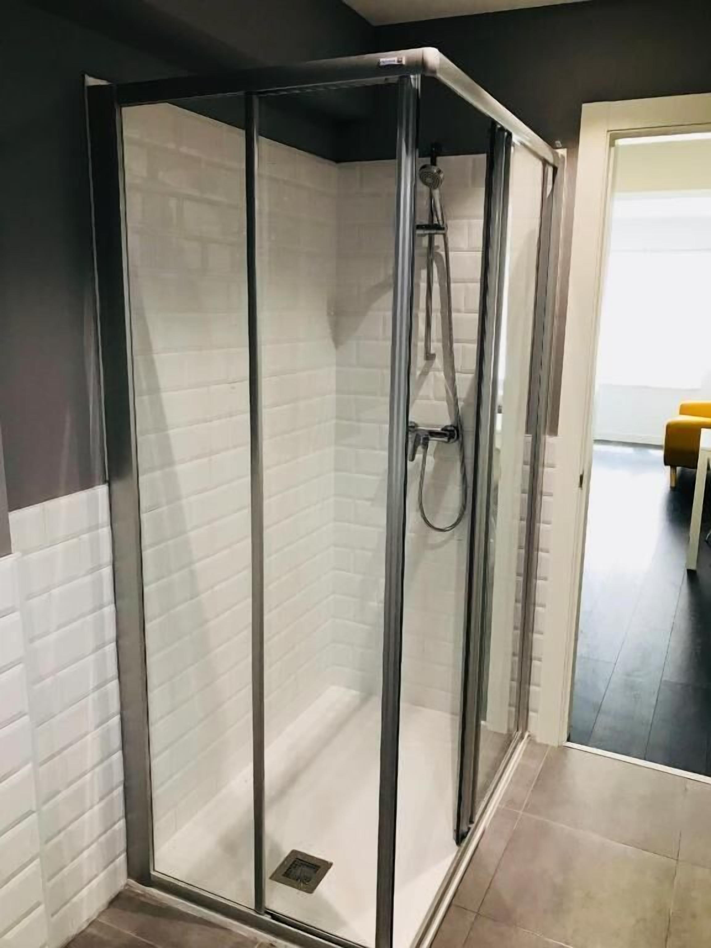 A glass-enclosed shower with a tiled wall and a showerhead.