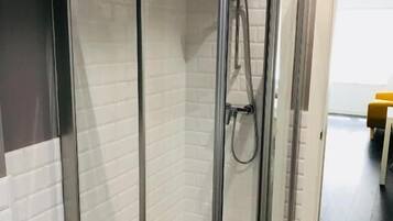 A glass-enclosed shower with a tiled wall and a showerhead.