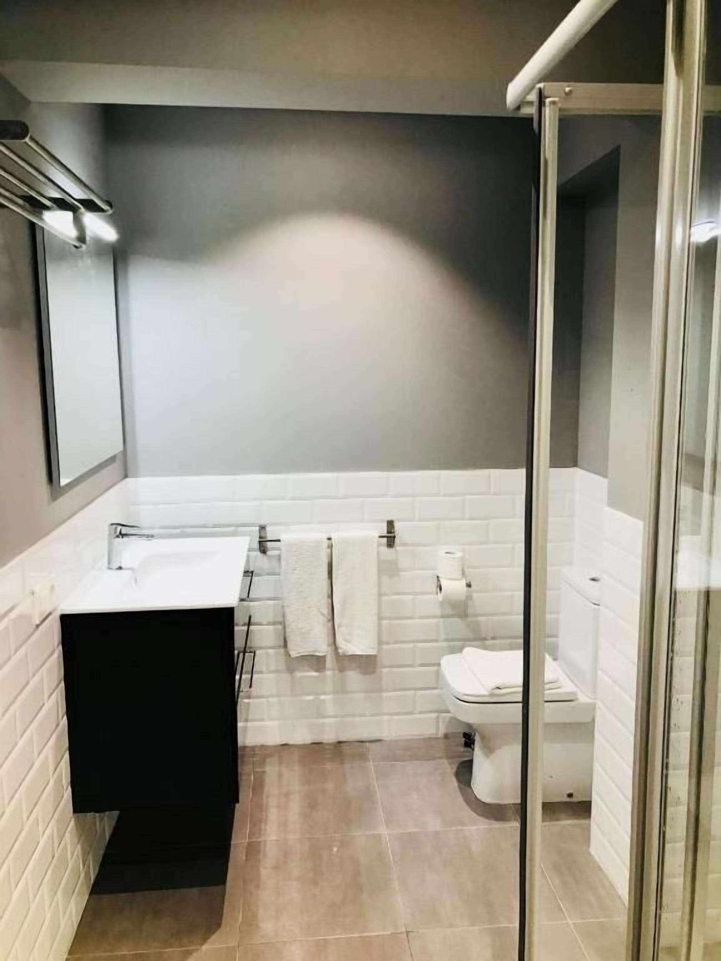 Un bagno moderno con un mobile lavabo nero, lavandino bianco e cabina doccia in vetro.