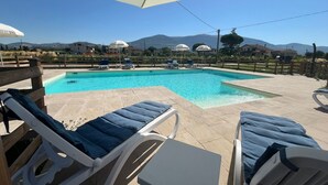A swimming pool with lounge chairs and umbrellas, surrounded by a wooden fence and a view of houses and mountains. - Luci di Assisi B&B Wellness (Assisi)