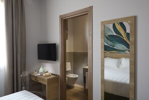 A hotel room with a wooden desk, a bed, a television, and a bathroom visible through an open door. - Luci di Assisi B&B Wellness (Assisi)
