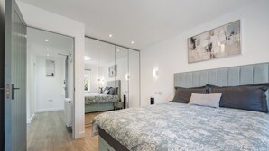 A modern bedroom with a large bed, a mirror, and a painting on the wall.