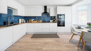 A modern kitchen with white cabinets, a blue backsplash, and a black range hood.
