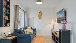 A modern living room with a blue sofa, a decorative leaf on the wall, a large window, and a cityscape painting.