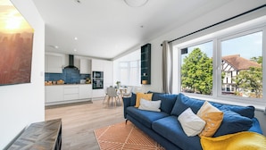 A modern living room with a blue sofa, a dining area, and a kitchen.