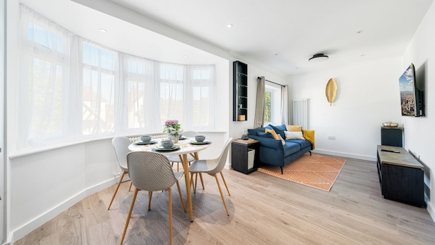 A modern living room with a dining area, large windows, and a city view.