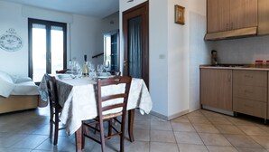 Zona de menjador amb taula preparada per a sis persones, cuina amb armaris de fusta i un rellotge a la paret.