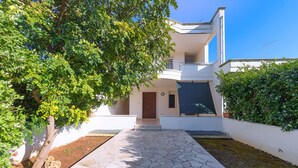 Una casa moderna de dos pisos amb un vestíbul pavimentat i un gran arbre al primer pla.