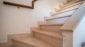 Una escala amb graons beix i barana de fusta, que porta a una plataforma amb una làmpada.