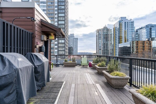A rooftop deck with outdoor furniture, planters, and a view of surrounding high-rise buildings. - Seattle's Gem: Elegant 1BR in Belltown - Sleeps 4 (Seattle)