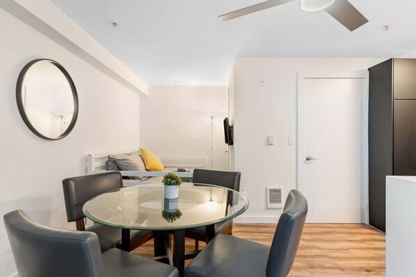 Un soggiorno moderno con un tavolo da pranzo in vetro, poltrone in pelle, uno specchio rotondo e una ventola a soffitto.