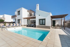 Una vila moderna amb piscina, mobiliari exterior i una pèrgola.
