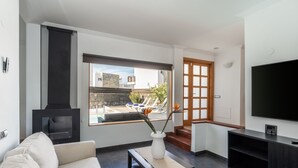 Ein modernes Wohnzimmer mit Kamin, großem Fenster mit Blick auf einen Pool, einer Couch, einem Couchtisch und einem Fernseher.