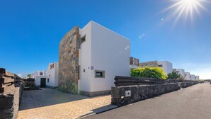 Ein modernes Gebäude mit Stein-Fassade und weißen Wänden, an einer gepflasterten Straße gelegen, mit blauem Himmel und Sonne im Hintergrund.